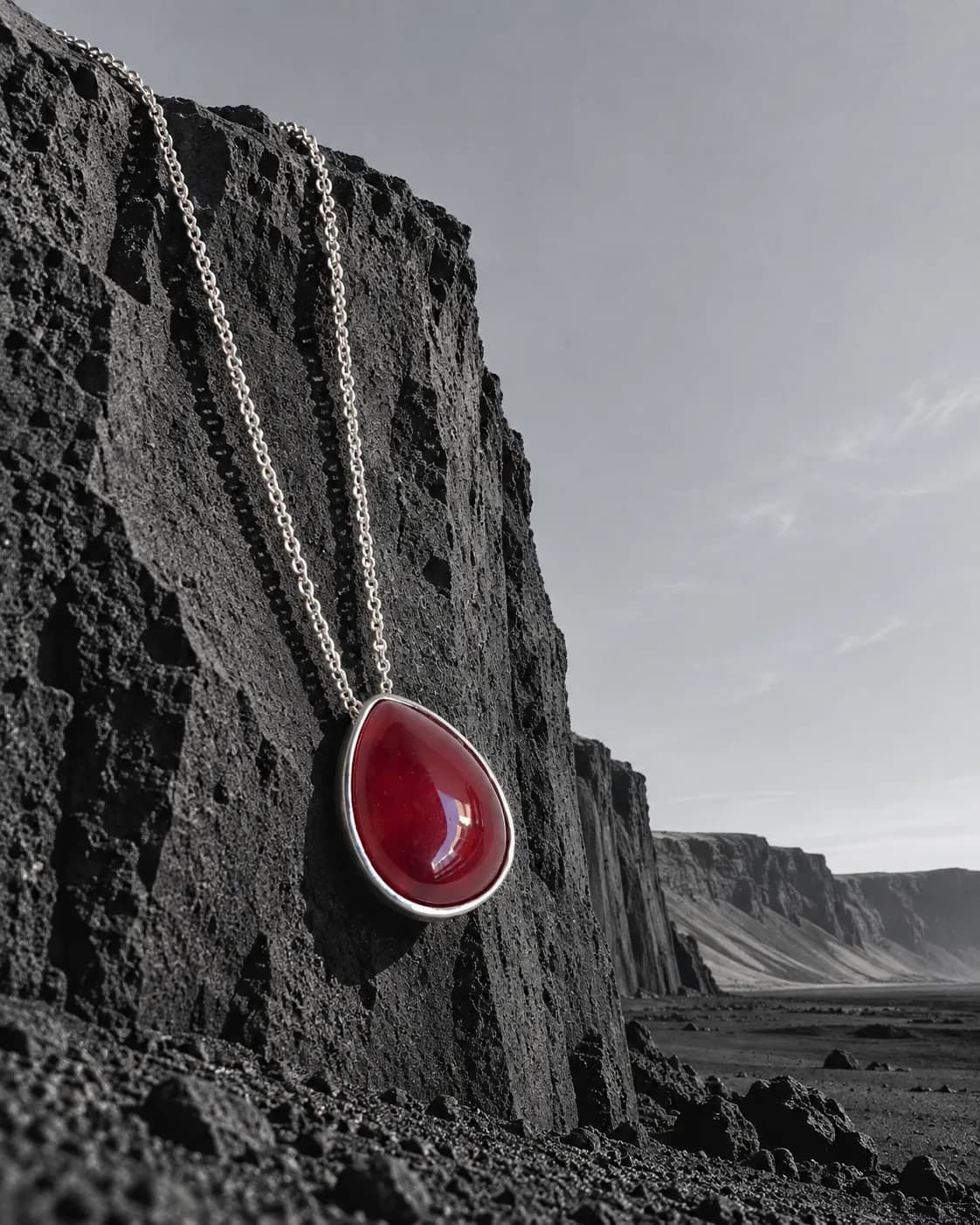 Colar com gota de jaspe vermelho pendurado na borda de um penhasco de basalto, em preto e branco